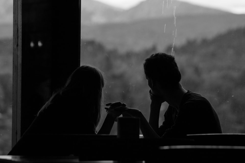 grayscale photography of couple sits by the window