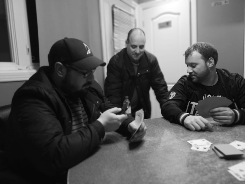 grayscale photography of three people playing cards
