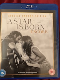 A Blu-ray case for the film 'A Star is Born: Encore' special edition features a grayscale image of a man and woman sitting closely, with the man playing a guitar. The top of the case has a blue banner indicating it's a Blu-ray disc, and there's a 15 age rating symbol on the lower left and right corners.