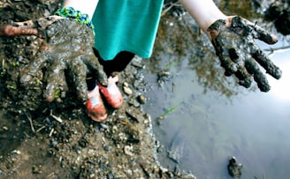 child in green top with mud on hand