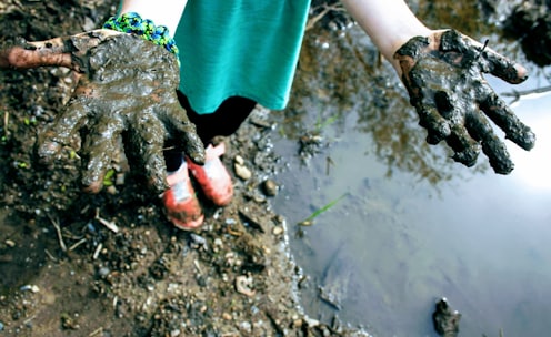 child in green top with mud on hand