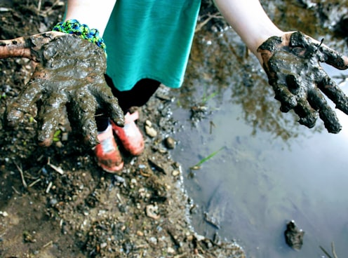 child in green top with mud on hand