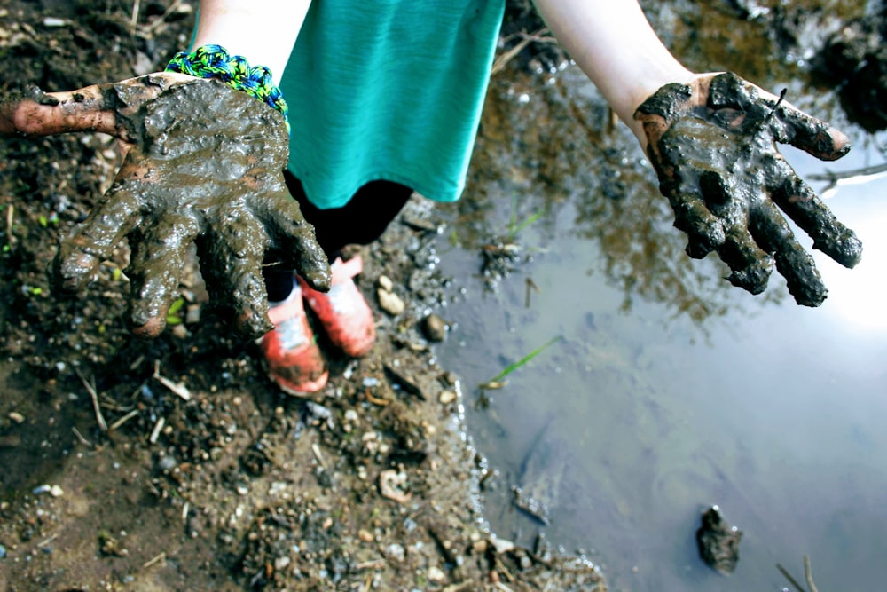 child in green top with mud on hand