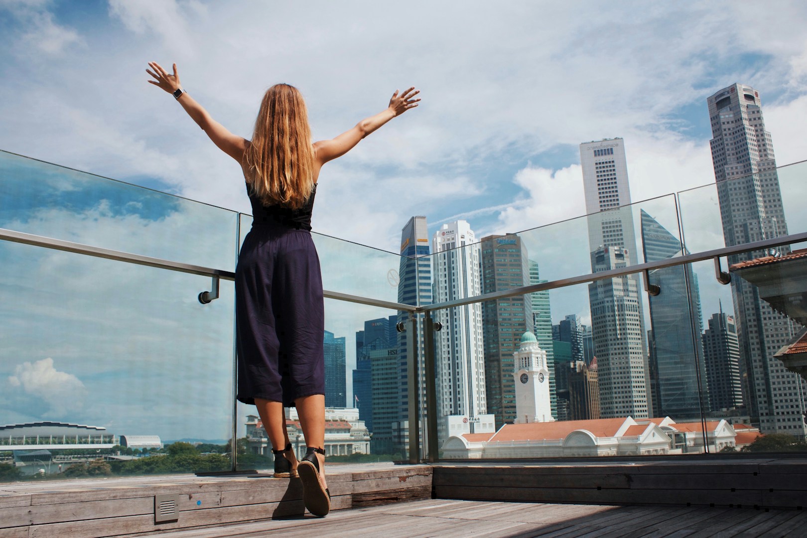 Woman raising her hands in celebration against a glass wall, symbolizing achievement and financial freedom