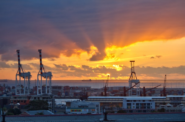 A vibrant port scene at sunset with containers and cargo ships in blue, green, and gray tones.