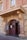 An entrance to a historic brick building featuring a curved archway with the words 'Court House' prominently displayed above a double wooden door. The architecture has ornate elements with a mix of stone and brick textures, and there are windows above the entrance.