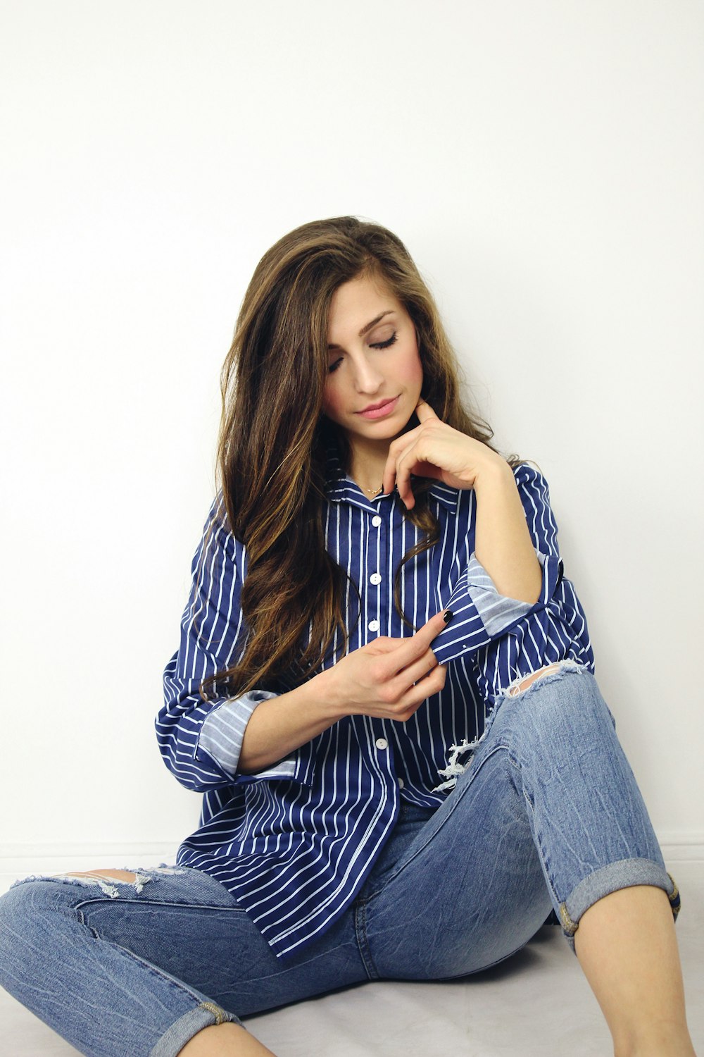 woman wearing blue and white striped dress shirt and blue denim jeans sitting on gray surface