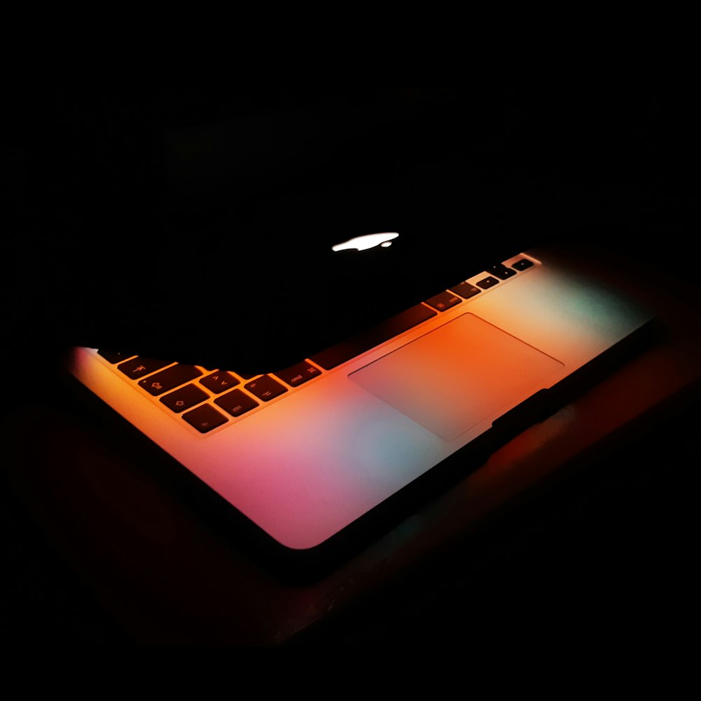 an apple laptop lit up in the dark