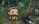 A Funko Pop figure with a yellow shirt and dark pants stands amidst tall, green grass. The background is a natural setting with blurred greenery, adding a sense of wilderness.