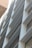 A modern building facade with a series of horizontal slats or louvers, creating a pattern of lines and shadows. The facade is composed of metallic and glass materials, reflecting light and capturing an urban architectural design.