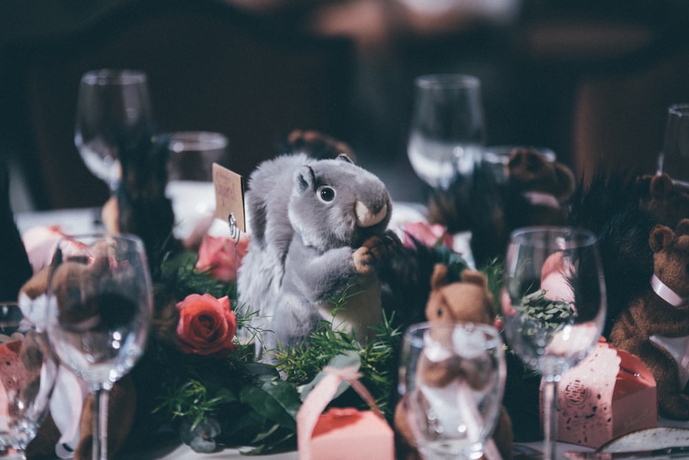 selective focus photography of squirrel toy surrounded by wine glasses