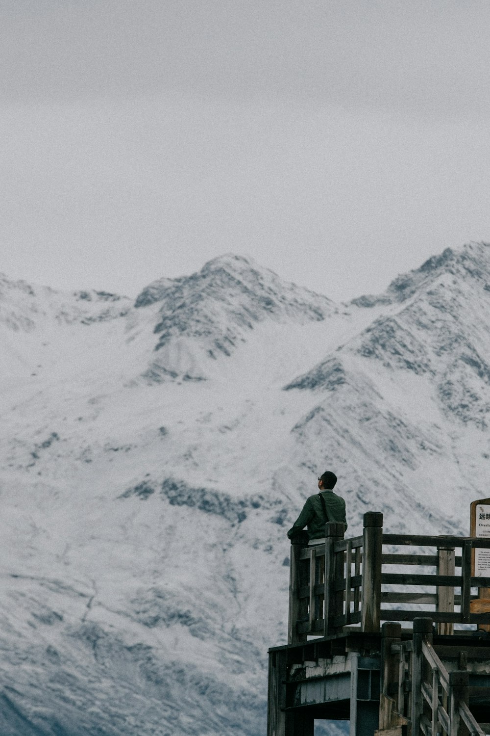 man standing on wooden terrace looking at mountain alps