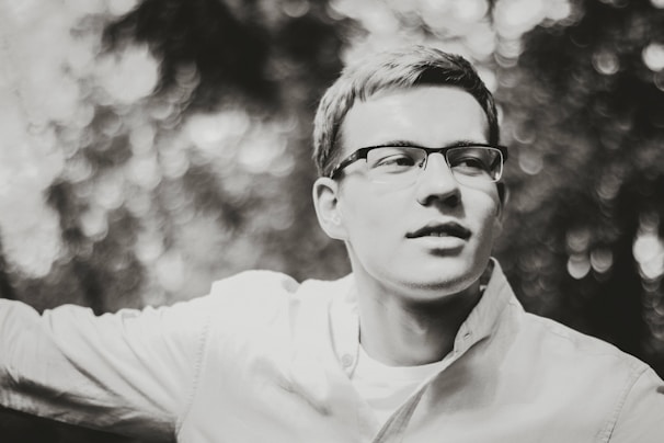 Portrait photo of a male elementary school teacher wearing glasses with a soft blue backdrop