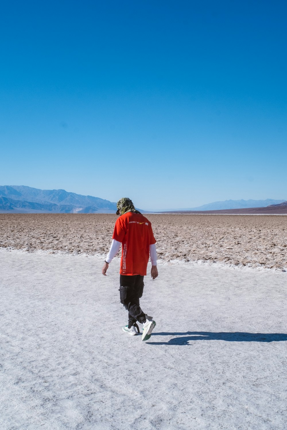 man wearing red and white shirt walking on sand