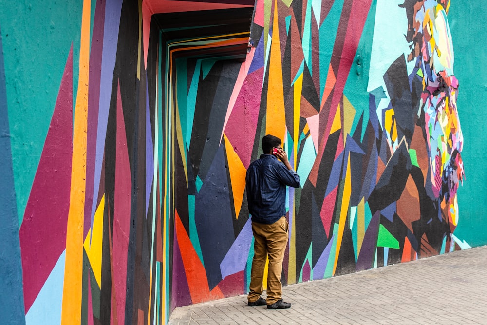 man wearing blue dress shirt and brown jeans standing beside of graffiti wall art