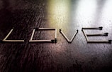 A series of matchsticks arranged to form the word 'LOVE' on a dark wooden surface. Each matchstick is carefully positioned to create the illusion of letters. The matches have blackened tips, suggesting they are unlit.