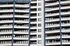 A modern apartment building with multiple floors, each featuring balconies with railings. The building has a repetitive architectural style with a mix of glass windows and white panels separated by vertical gray columns.