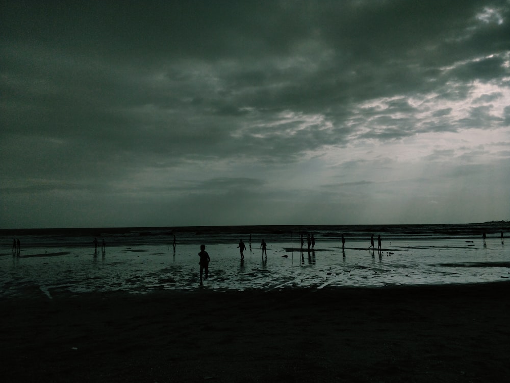 a group of people standing on top of a beach under a cloudy sky