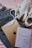 A pair of white sneakers with brown accents, a travel book with a geometric world map design, an Apple iPad, and a pair of blue jeans are laid out on a pink fabric background.