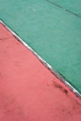 Aerial view of a court surface divided diagonally into two contrasting colors, green and red, separated by a thin silver strip.
