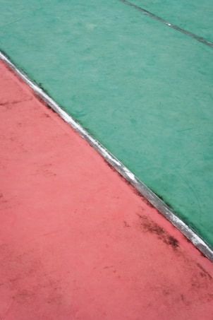 Aerial view of a court surface divided diagonally into two contrasting colors, green and red, separated by a thin silver strip.