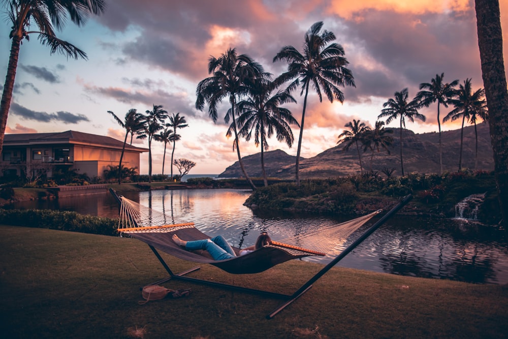 person on brown hammock with steel base across body of water