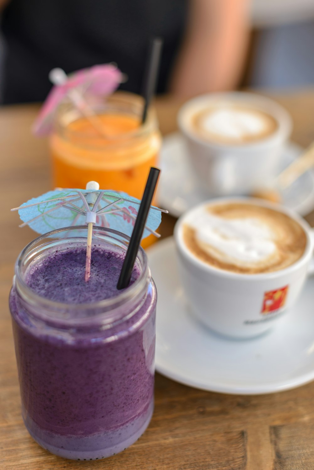 two orange and purple beverage in jar with small umbrella beside coffee latte