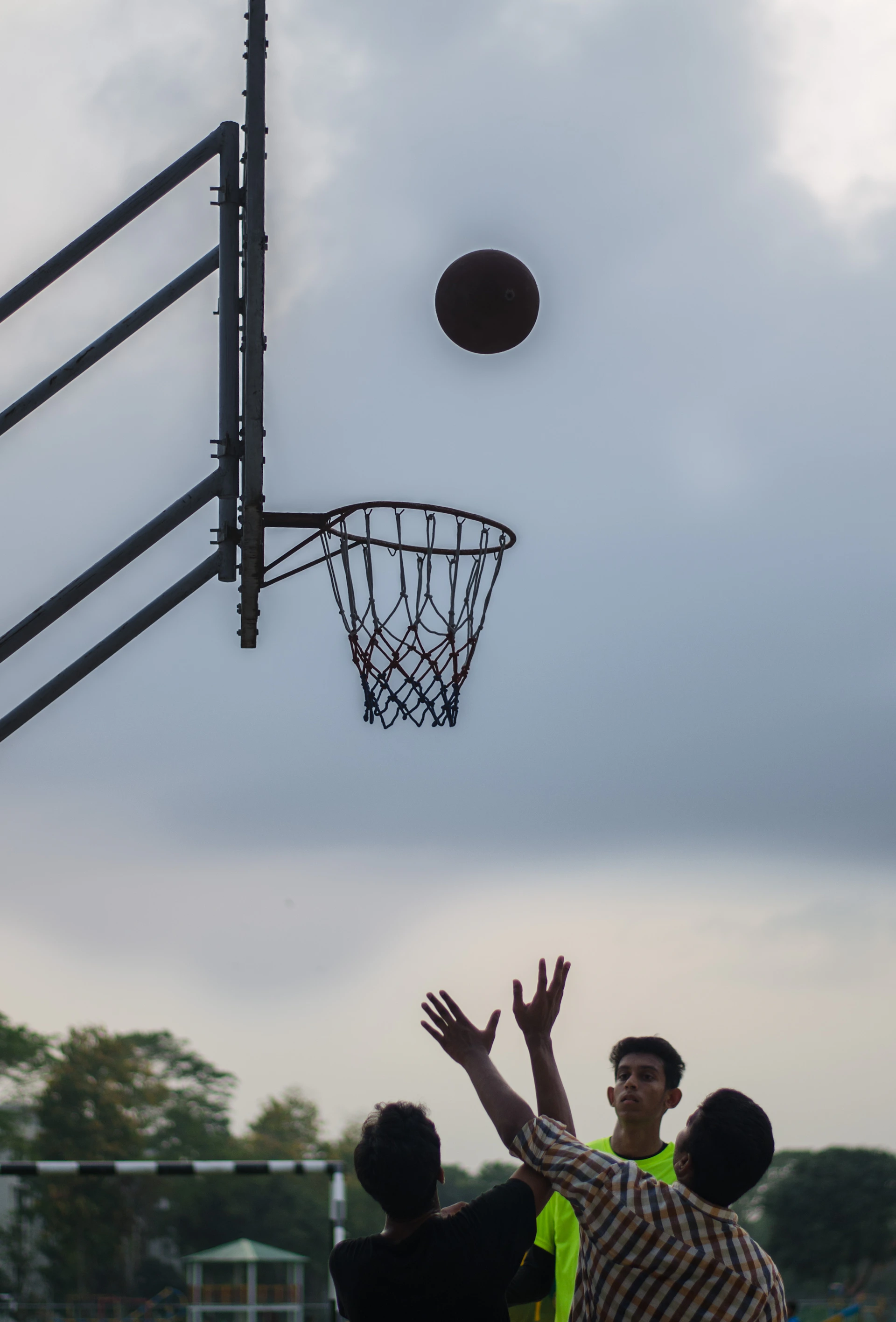 Dynamic action shot of a 3v3 basketball game in progress on an outdoor court, capturing players mid-jump and the ball soaring toward the hoop under bright daylight.