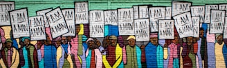 A mural depicting a group of people holding signs that read 'I Am A Man'. The figures are diverse, with a variety of clothing styles and colors. The background is composed of brick, and the mural uses vibrant, bold colors, emphasizing unity and strength.