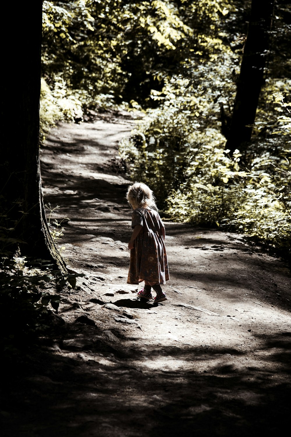 girl walking on soil road near shrubs and trees during day