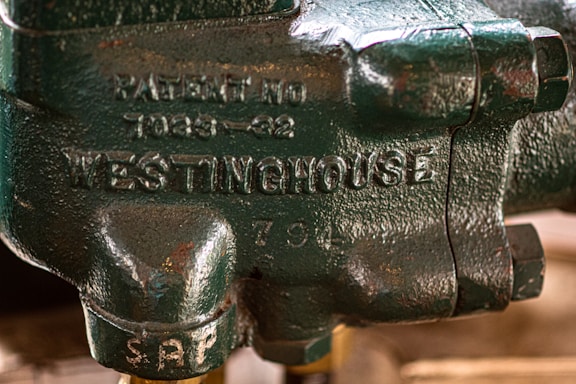 A close-up view of a green metallic component with inscriptions including 'WESTINGHOUSE' and a patent number. The surface has a textured finish with visible bolts.