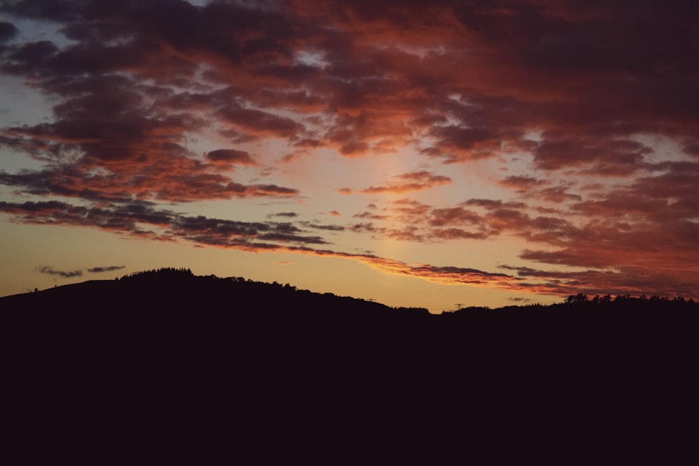 silhouette photography of mountain under cloudy sky during golden hour