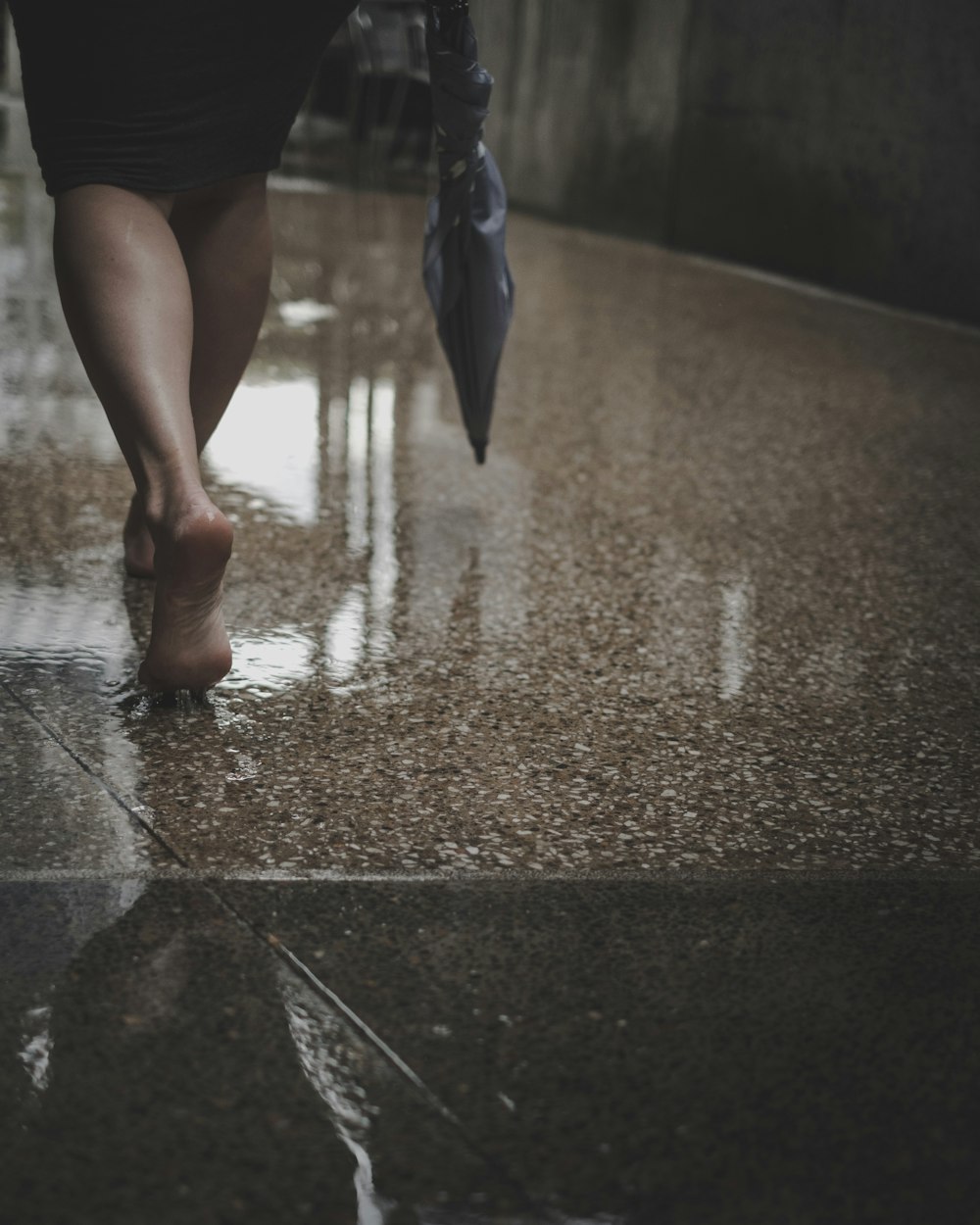 woman with umbrella on hand walking barefooted on wet floor