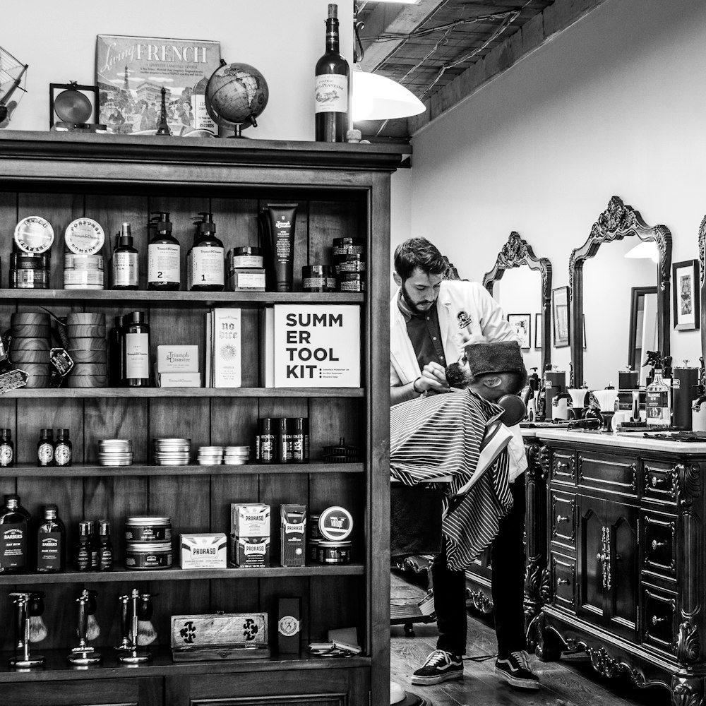 grayscale photography of barber shaving another man's chin