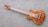 A wooden electric guitar with a natural finish rests on a textured gray carpet. It features a glossy body with intricate wood grain patterns and metallic hardware components such as pickups and control knobs. The guitar neck contains distinct red fret markings.