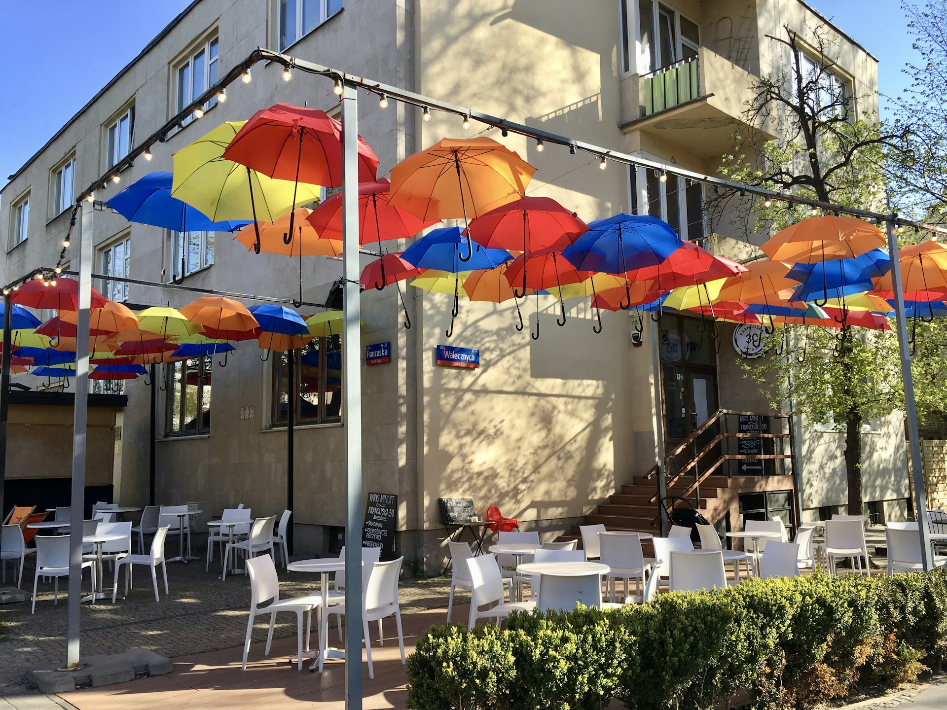 A vibrant street view of a Munich restaurant with outdoor seating under blue and white umbrellas on a sunny day.