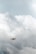 A drone is flying in a cloudy sky, surrounded by large, thick clouds that dominate the background. The drone is small in size compared to the vast expanse of clouds, suggesting it is at a considerable height.