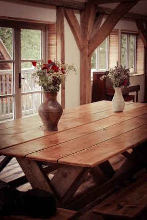 A rustic wooden dining table set with simple ceramic dishes and a vase of fresh wildflowers.