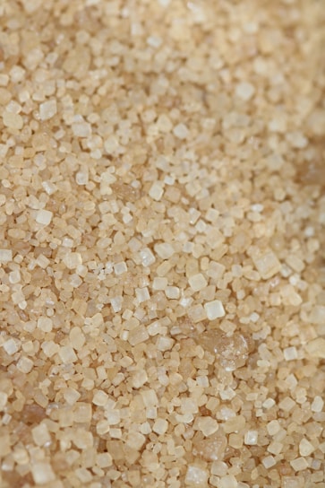 Close-up of golden coconut sugar crystals spilling from a rustic wooden bowl on a dark textured surface.