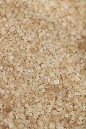 Close-up view of a large quantity of brown sugar crystals. The sugar granules are small, cube-like, and vary in shades from light tan to medium brown. The texture appears rough and granular.