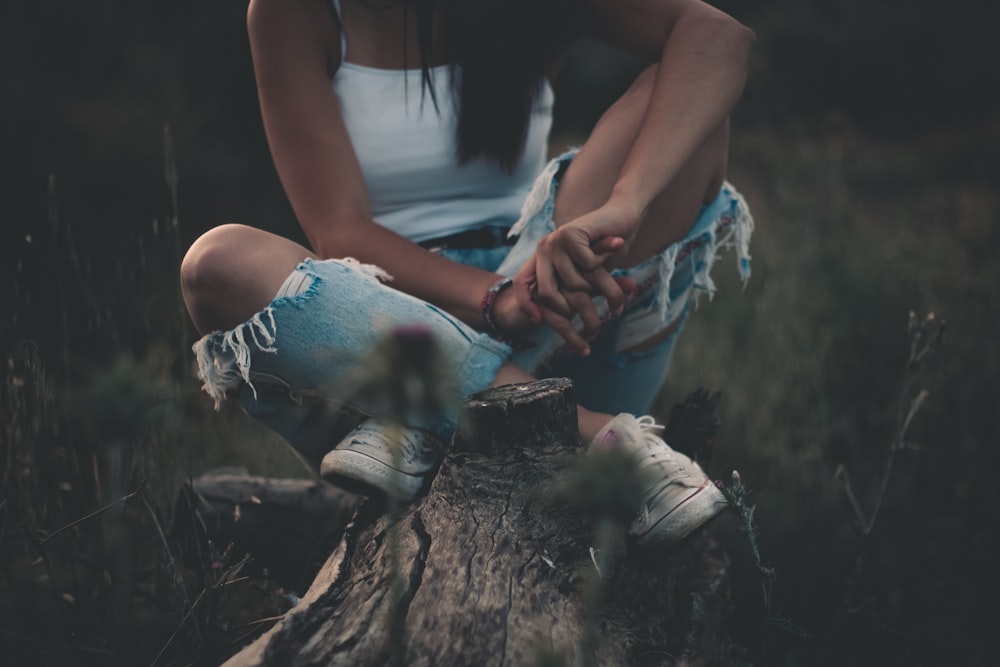 woman wearing blue denim distressed jeans sitting on tree trunk