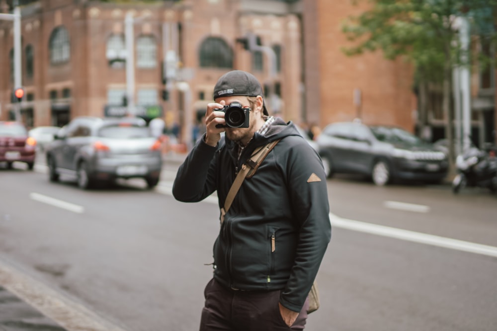 uomo che indossa una felpa con cappuccio nera che tiene la macchina fotografica mentre scatta una foto