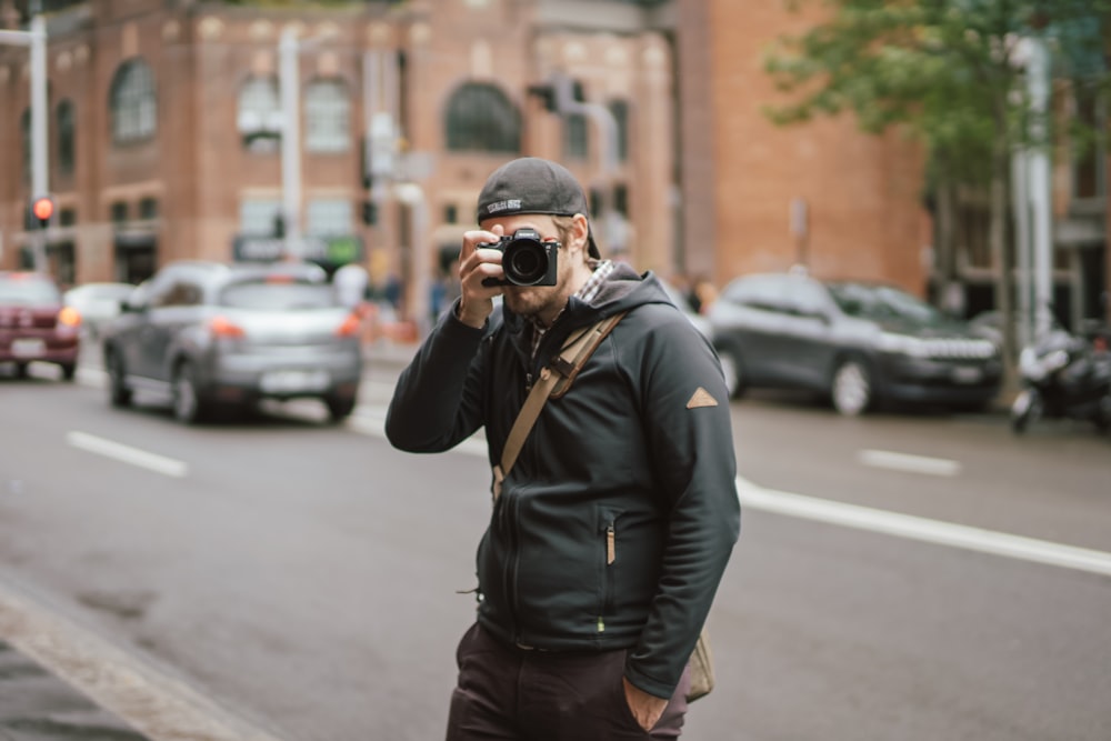 man wearing black hoodie holding camera while taking a picture