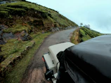 A winding road through lush green hills with a Prayog Travels vehicle cruising along.