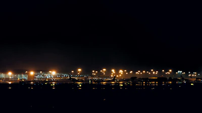 Night view of an airport cargo area with planes and containers illuminated by soft lights.
