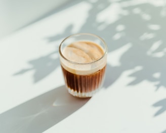 clear drinking glass with coffee on top of white table