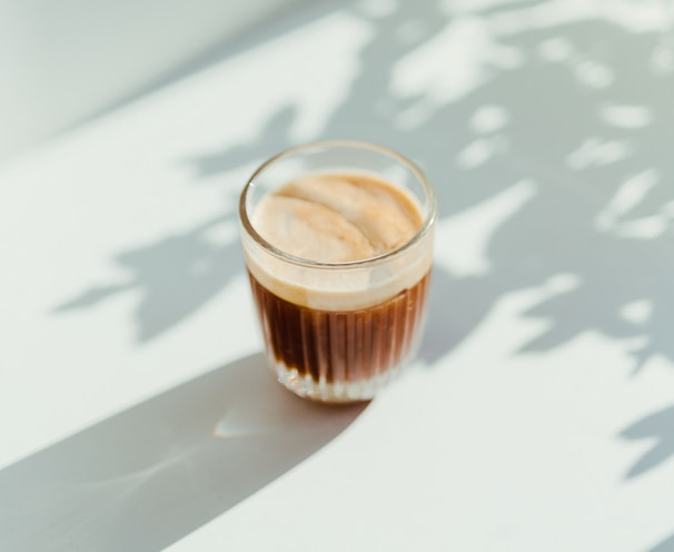 clear drinking glass with coffee on top of white table