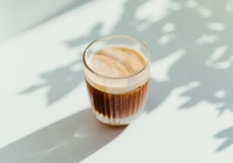 clear drinking glass with coffee on top of white table