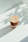 clear drinking glass with coffee on top of white table