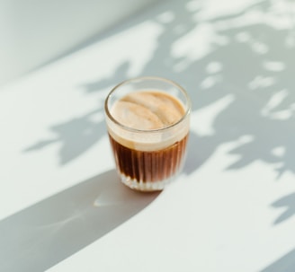 clear drinking glass with coffee on top of white table